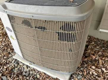 A damaged outdoor Carrier AC unit with bent fins, indicating a need for HVAC repair or service by Omaha Heating and Air in Omaha, NE.