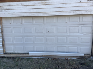A damaged residential garage door in need of repair or replacement by Horton & Hill Garage Door Specialists LLC in Sapulpa, OK.