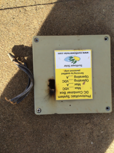 A damaged solar DC combiner box with burnt wires, indicating a repair job by Watts Happening Electric in Lakewood, CO.