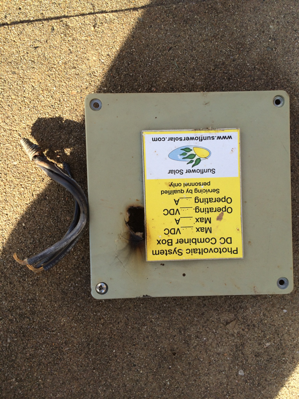 A damaged solar DC combiner box with burnt wires, indicating a repair job by Watts Happening Electric in Lakewood, CO.
