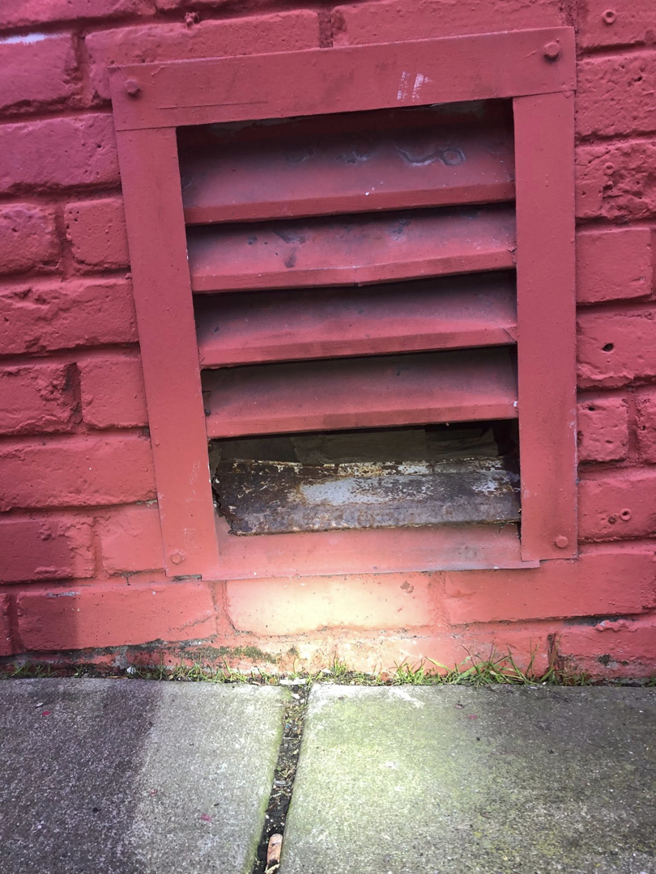 A damaged vent on a red brick wall, indicating a potential pest entry point, inspected by Sophie's Pest Solutions in Oakland, CA.