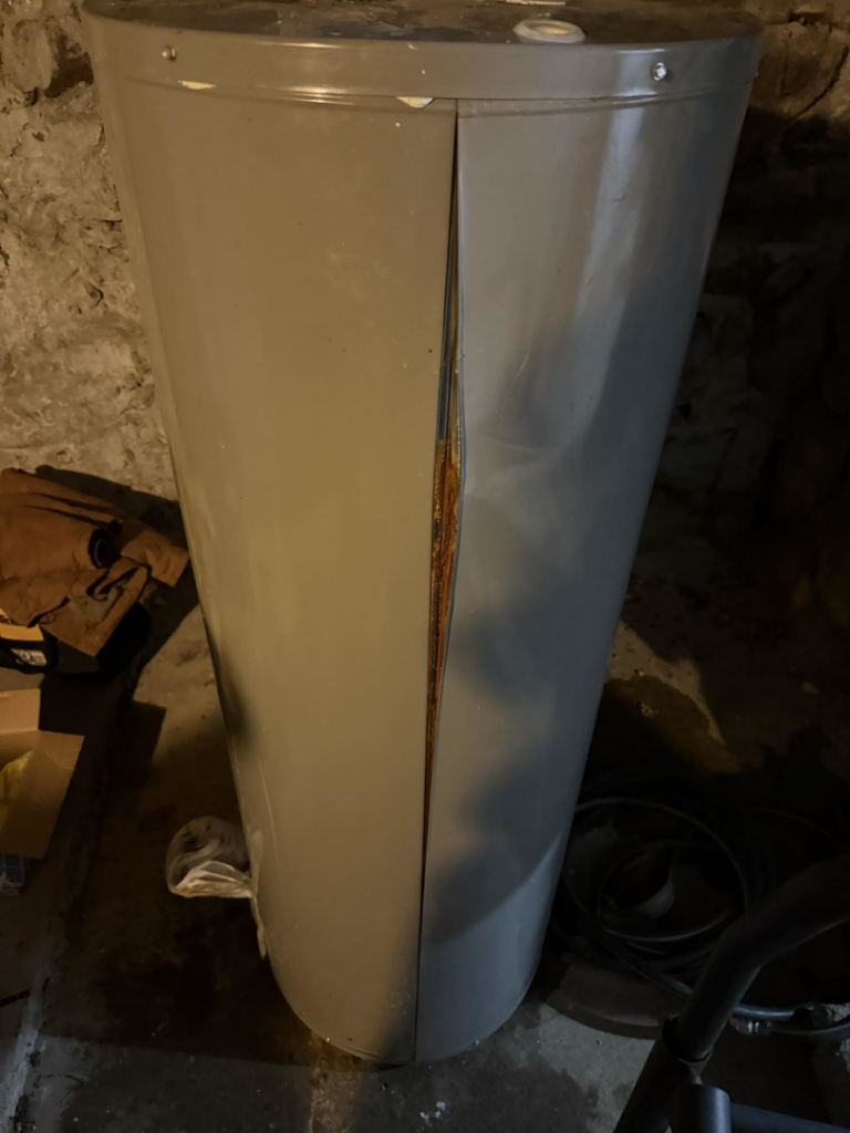 A severely damaged water heater in a basement, indicating a need for service from Wright Mechanical in Ypsilanti, MI.