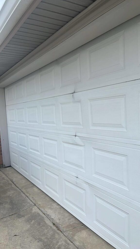 A damaged white garage door showing dents, ready for repair by Legacy Garage Doors & Repairs in Church Point, LA.