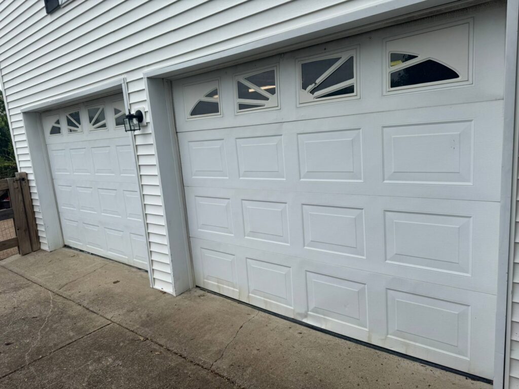 Two white panel garage doors on a residential home, one showing a damaged panel, ready for repair by Swift Garage Door in Nashville, TN.
