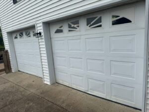Two white panel garage doors on a residential home, one showing a damaged panel, ready for repair by Swift Garage Door in Nashville, TN.