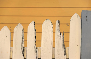 A close-up of a damaged white picket fence, showing potential repair work by Palmetto Fence Co in North Charleston, SC.