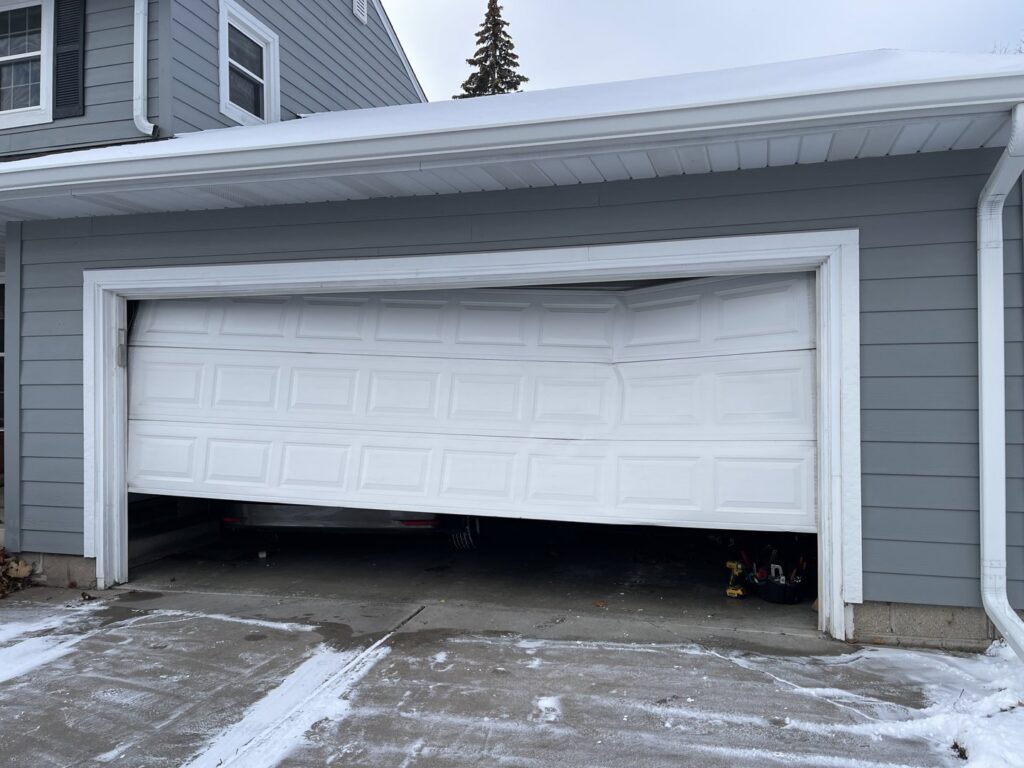 A severely damaged white residential garage door, bent inwards, requiring repair or replacement by Max Garage Door in Minneapolis, MN.