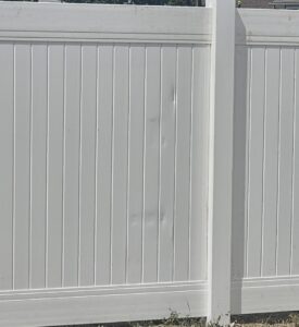 A close-up of a white vinyl privacy fence panel showing minor damage, installed by All American Vinyl in Provo, UT.