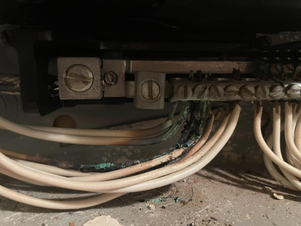 Close-up of damaged and corroded wiring inside an electrical panel, indicating repair work by Charging Rhino Electric in Mobile, AL