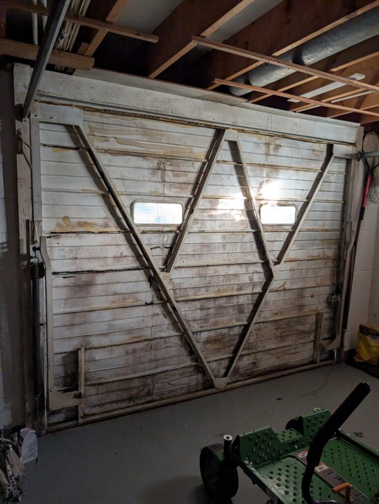 An old, damaged wooden garage door in need of repair or replacement by Gilliam Services LLC in Johnson City, TN.