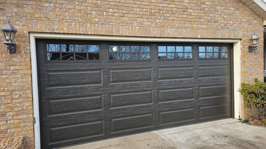 A dark brown garage door with decorative windows on a brick house, installed by A+ Garage Door Repair in Evansville, IN.
