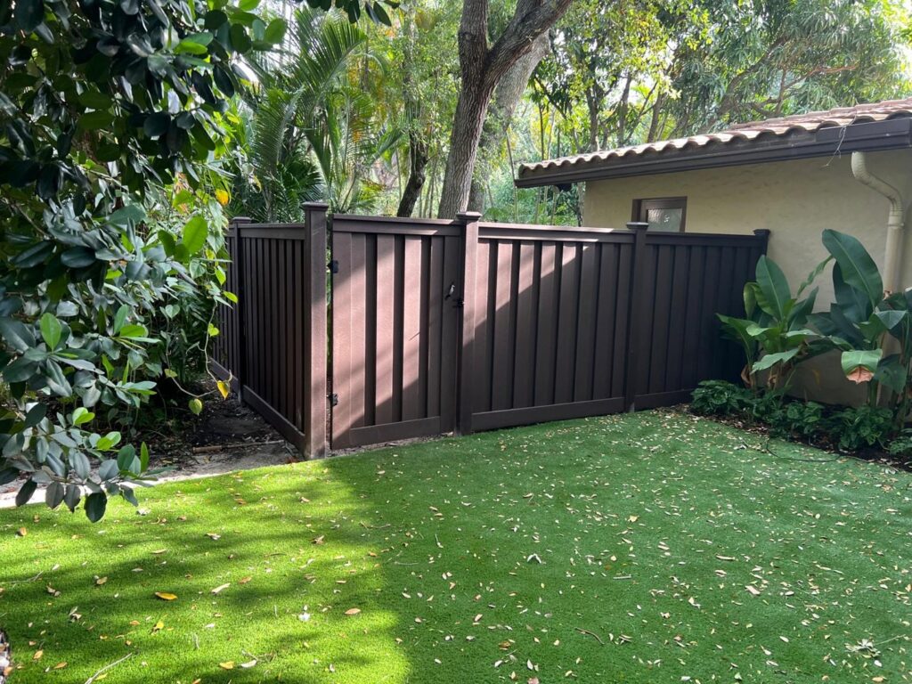 A dark brown privacy fence with a gate installed in a lush backyard by Palm's Fence of Miami, FL.