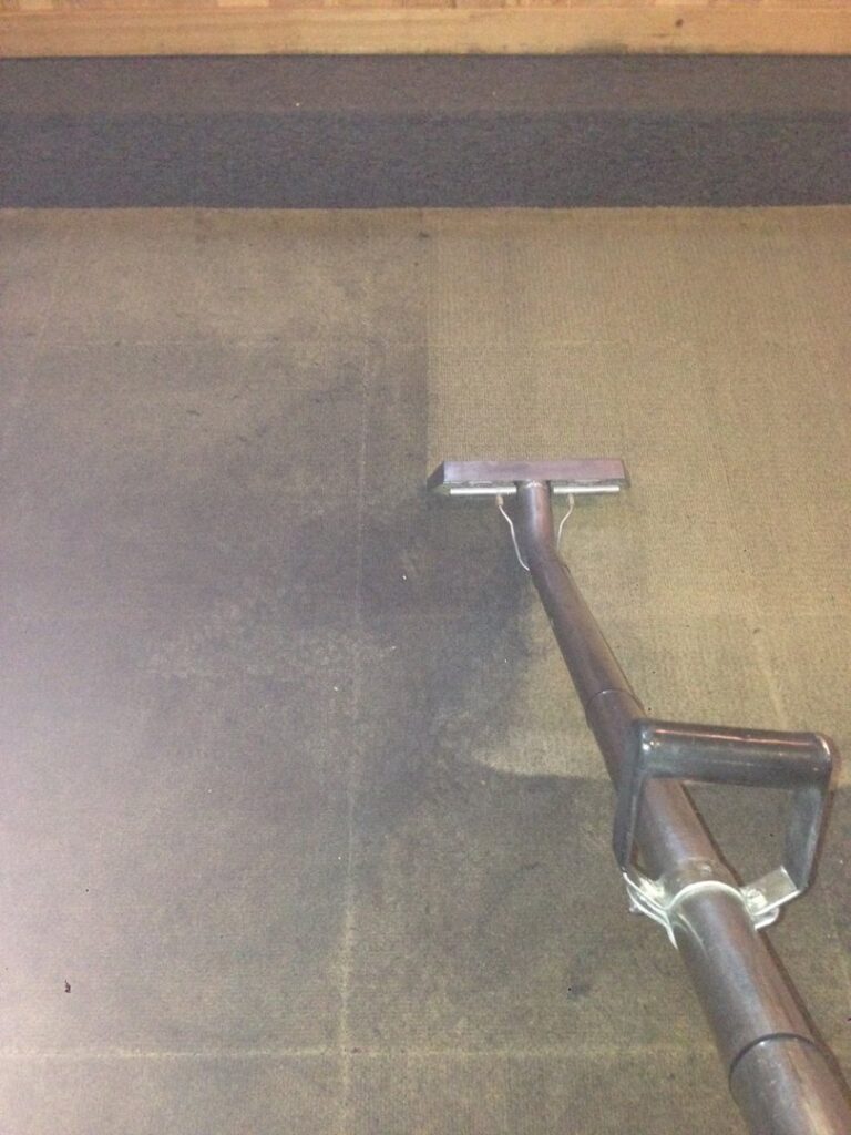 A dark carpet showing a clear before and after cleaning result with a cleaning wand by Radiant Rugs Carpet Cleaning in Spokane, WA.