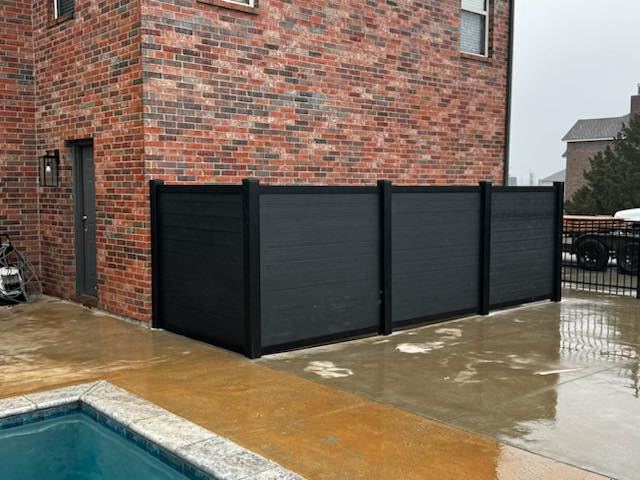 A dark composite privacy fence installed poolside by Goliath Fence Systems and Pre-Stain in Oklahoma City, OK.