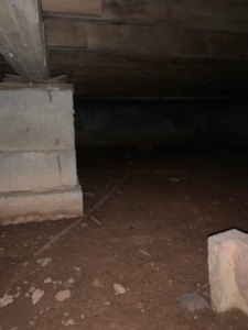 A dark crawl space with a dirt floor and concrete piers, typical for pest inspections by Buzz Pest Control in Springfield, MO.