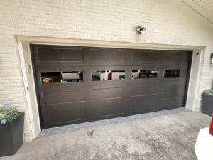 A modern dark garage door with upper windows, installed on a white brick house by Knox Garage Door Service LLC in Knoxville, TN.