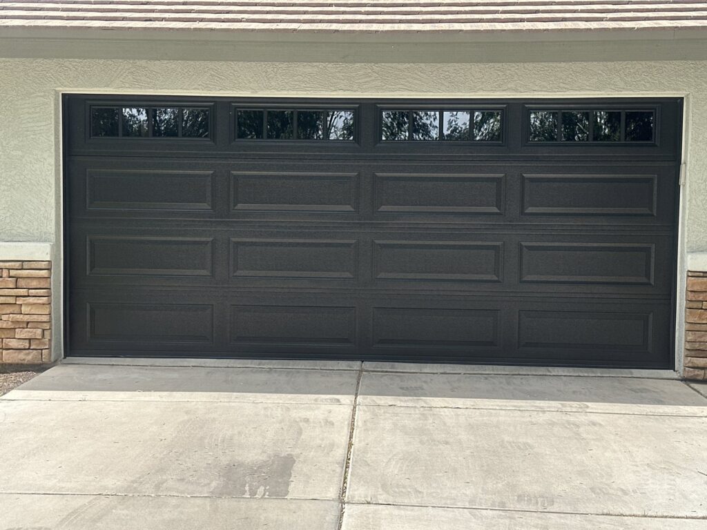 A modern dark gray panel garage door with top windows and stone accents, installed by JT's Overhead Doors in Gilbert, AZ.