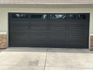 A modern dark gray panel garage door with top windows and stone accents, installed by JT's Overhead Doors in Gilbert, AZ.