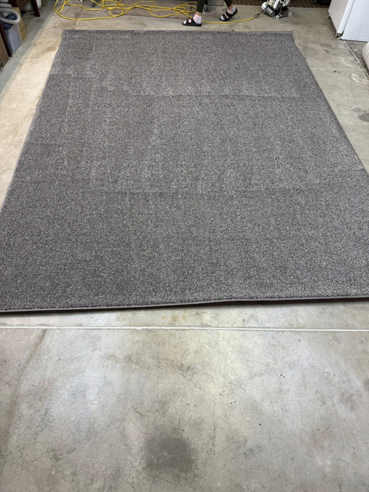 A dark grey area rug with visible seams, indicating custom work by Rug Edge Binding Company in Spokane, WA