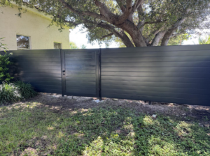 A newly installed dark grey horizontal slat fence with a matching gate in a residential backyard by HD Multi Service USA INC in Miami, FL.