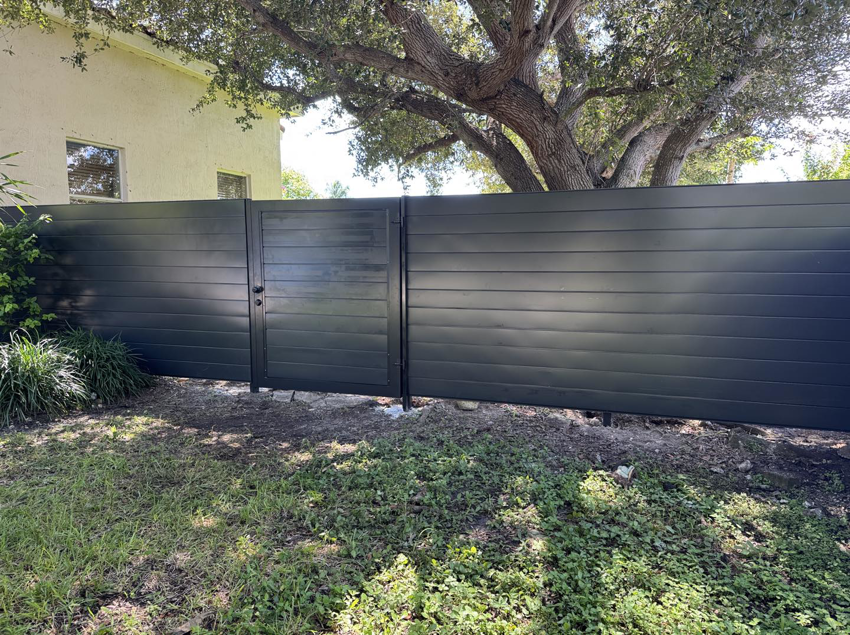 A newly installed dark grey horizontal slat fence with a matching gate in a residential backyard by HD Multi Service USA INC in Miami, FL.
