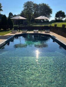 An inground pool featuring a dark liner, concrete decking, and patio umbrellas, a project by Riverstone LLC in Bowling Green, KY.