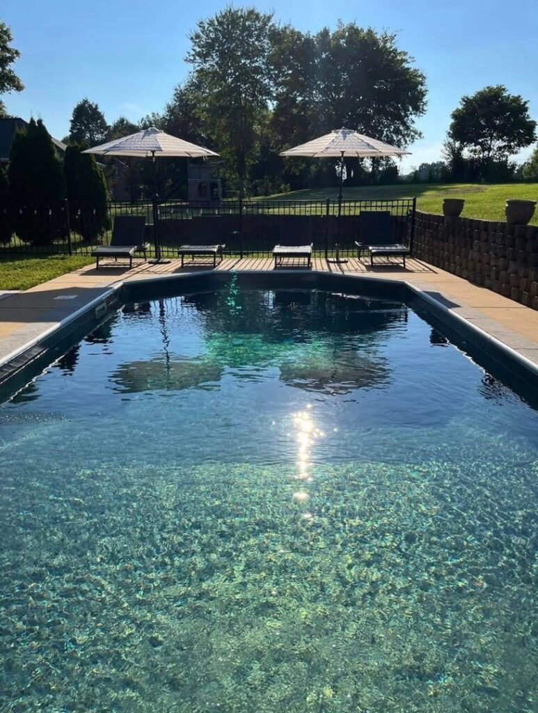 An inground pool featuring a dark liner, concrete decking, and patio umbrellas, a project by Riverstone LLC in Bowling Green, KY.