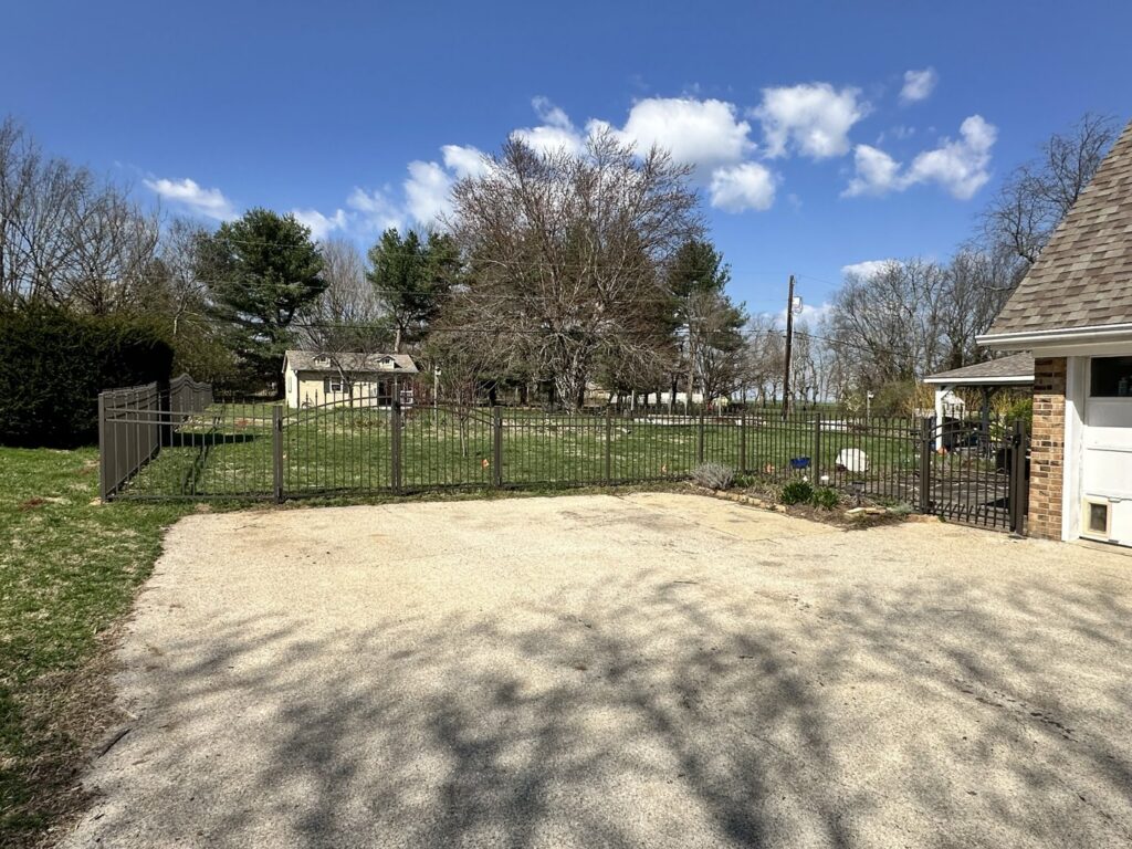 A dark metal fence installed around a large gravel driveway and yard by Border Built Fencing in Florence, KY.