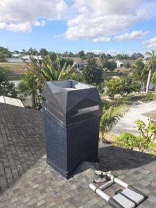 A dark modern chimney cap installed on an asphalt shingle roof by SWFL Chimney Caps Inc. in Fort Myers, FL.