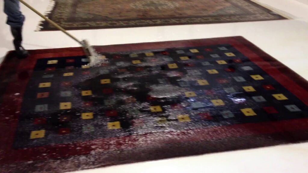 A dark patterned rug being cleaned with a scrub brush and water at Renaissance Rug Cleaning Inc. in Portland, OR.