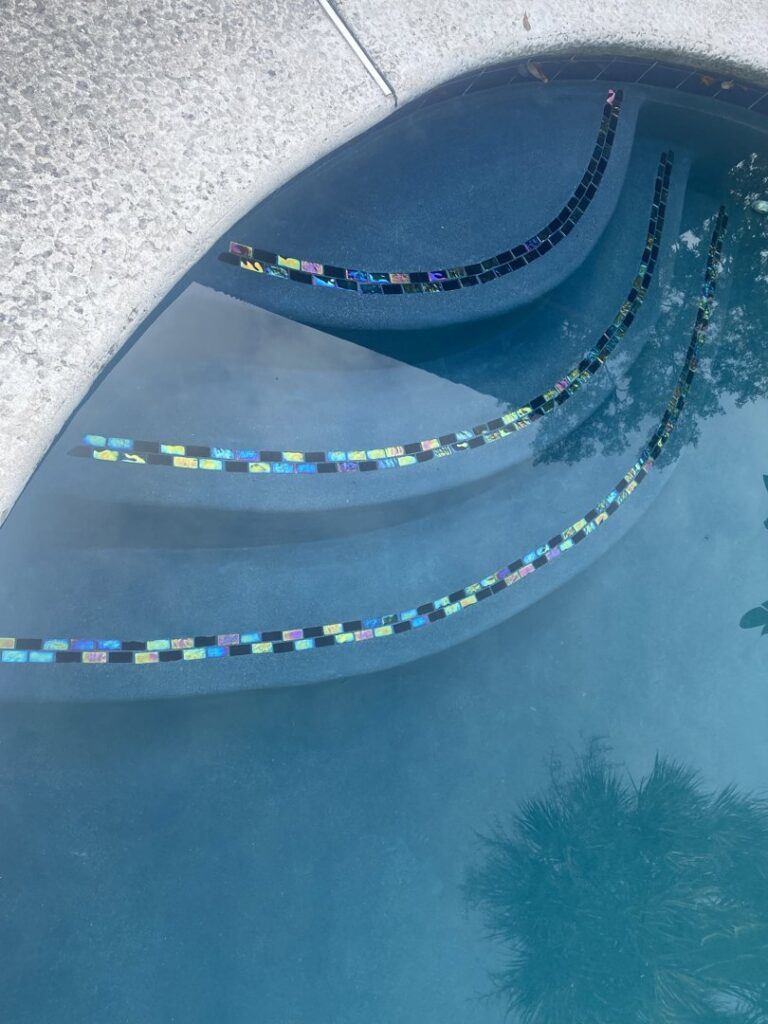 Dark-bottomed pool steps featuring iridescent mosaic tiles, a custom finish by I10 Pool Plastering LLC in Kenner, LA.