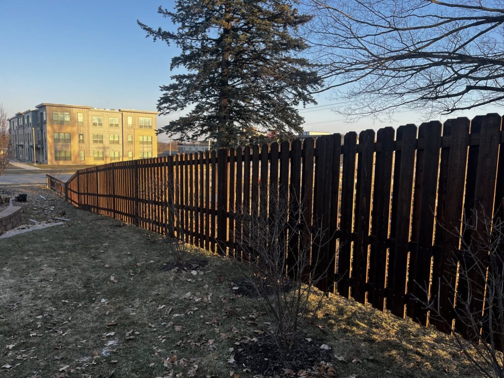A dark stained wooden picket fence running alongside a street by Brothers Fence Co. in Madison, WI.