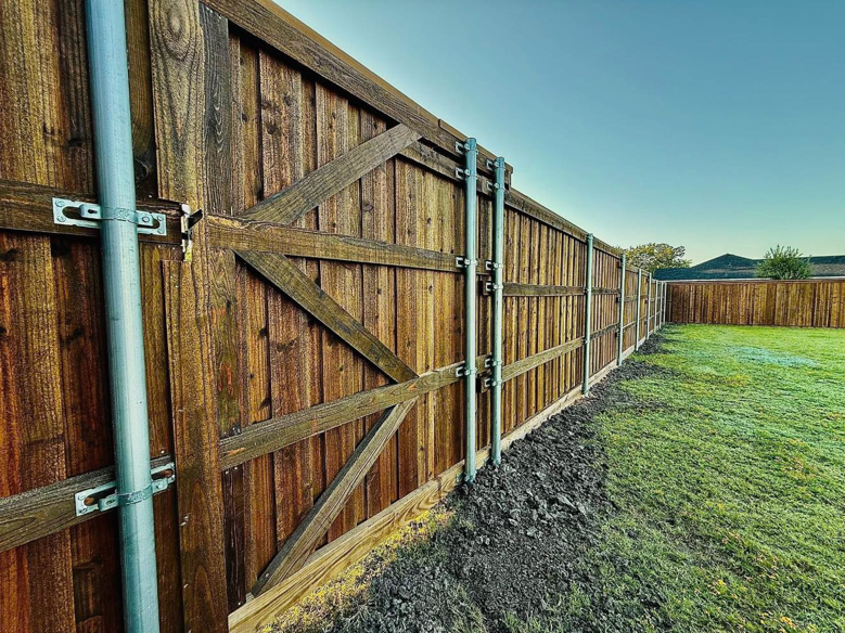 A newly installed dark-stained wooden fence with a matching gate and metal posts by CW Fence and Fab in Forney, TX.