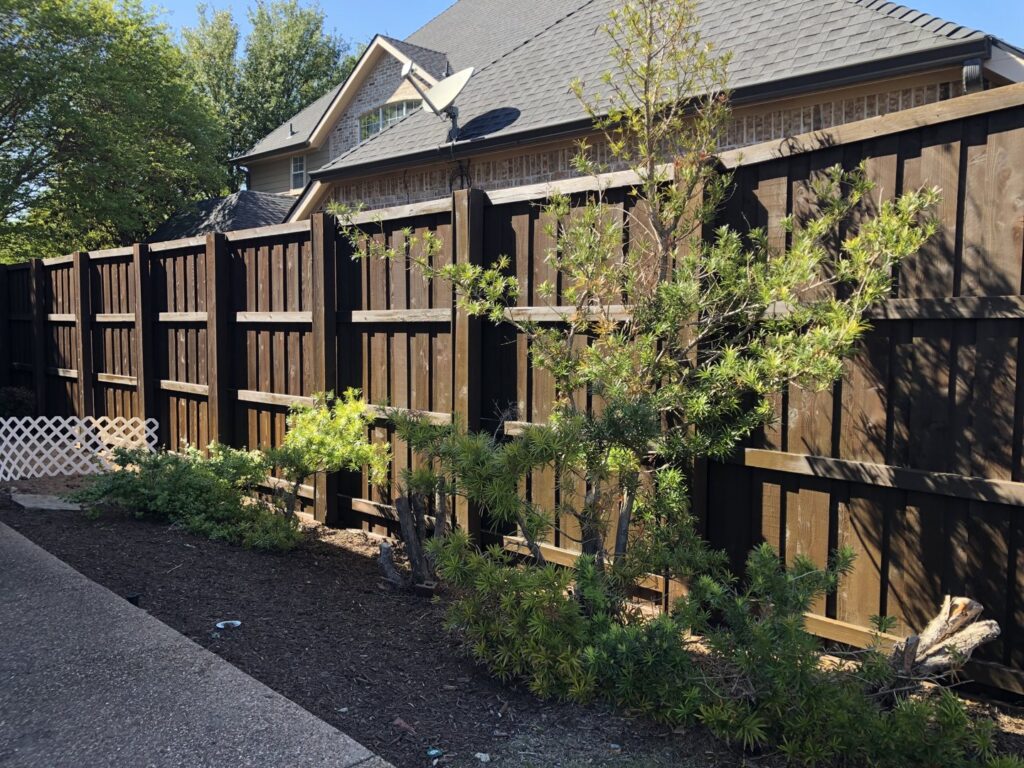 A dark stained wood fence with landscaping in a residential backyard by Fence Defense in Plano, TX