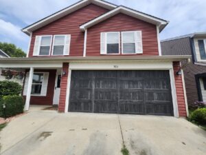 A dark, weathered-look garage door installed on a red house by Steve's Overhead Door Company in Lafayette, IN.