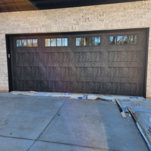 A dark wood-look garage door with top windows installed on a brick home by Getsinger's Overhead Doors in Spartanburg, SC.