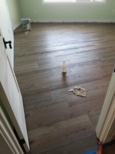 A room showcasing a dark wood plank flooring installation, with cleaning supplies on the floor, completed by LACarpetWarehouse in Los Angeles, CA.