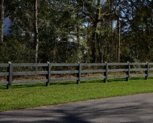 A dark-stained wooden split-rail fence running alongside a grassy area and road, installed by Five Star Fence in Charleston, SC.