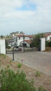 A decorative black metal gate with white pillars at a residential entrance by Automated Entry Systems Inc in Escondido, CA.