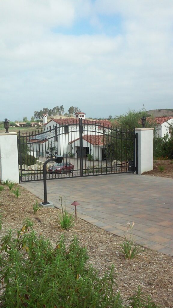 A decorative black metal gate with white pillars at a residential entrance by Automated Entry Systems Inc in Escondido, CA.
