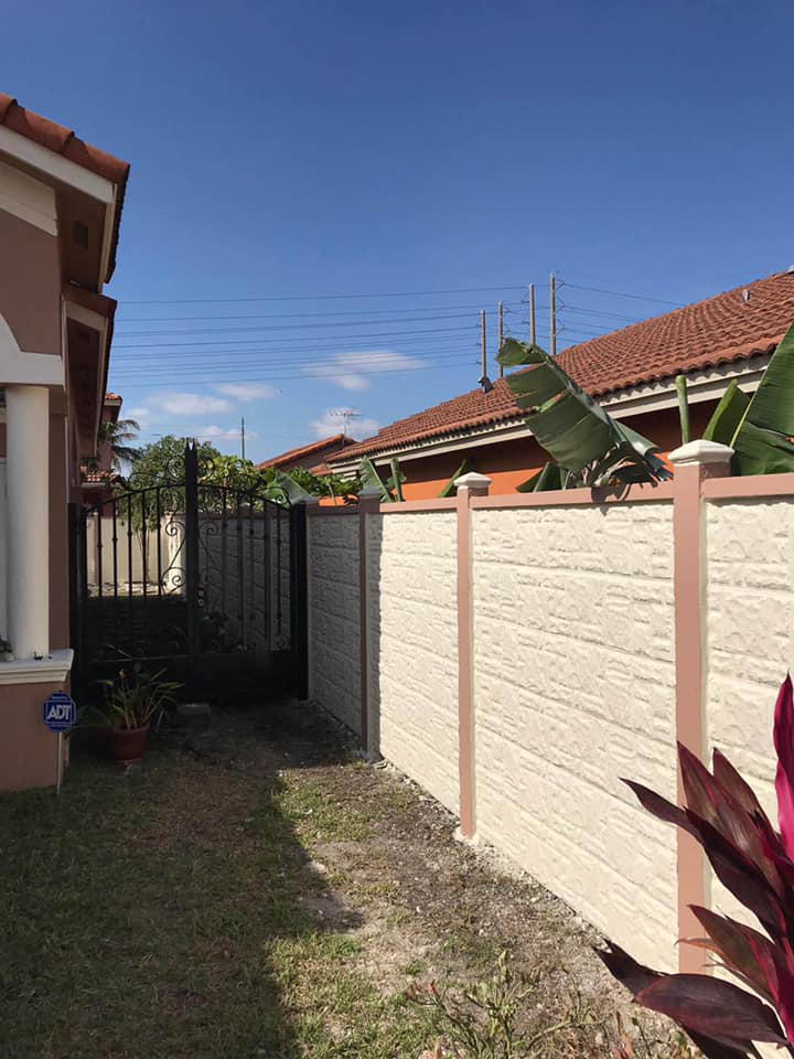 A decorative concrete fence and metal gate installed in a side yard by Miami Concrete Fence in Miami, FL
