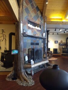 A decorative fireplace with a stone and wood surround on display in the showroom of Wood Stoves For Sale in Fairbanks, AK.