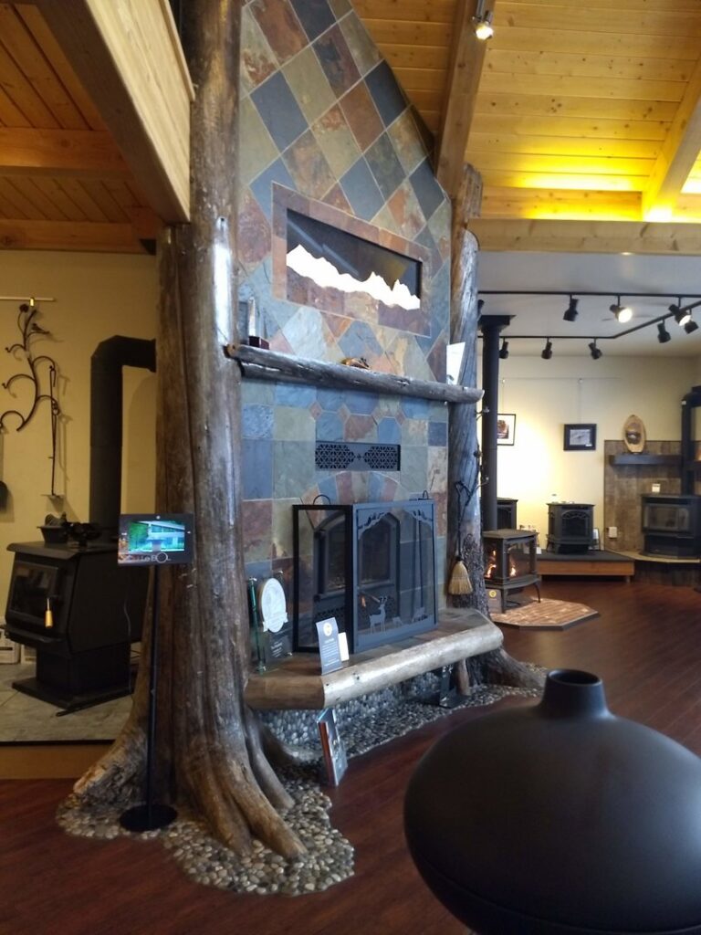 A decorative fireplace with a stone and wood surround on display in the showroom of Wood Stoves For Sale in Fairbanks, AK.