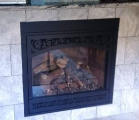 A gas fireplace insert with ornate decorative trim and burning logs, installed by North Central Service, Inc. in Minot, ND.