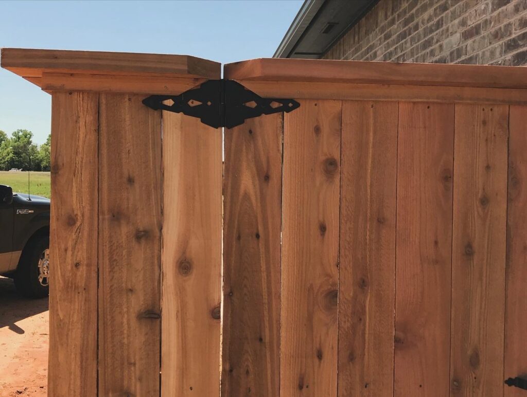 A close-up of a wooden fence gate featuring a decorative black hinge, installed by 12 Corners Fence Company in Tecumseh, OK