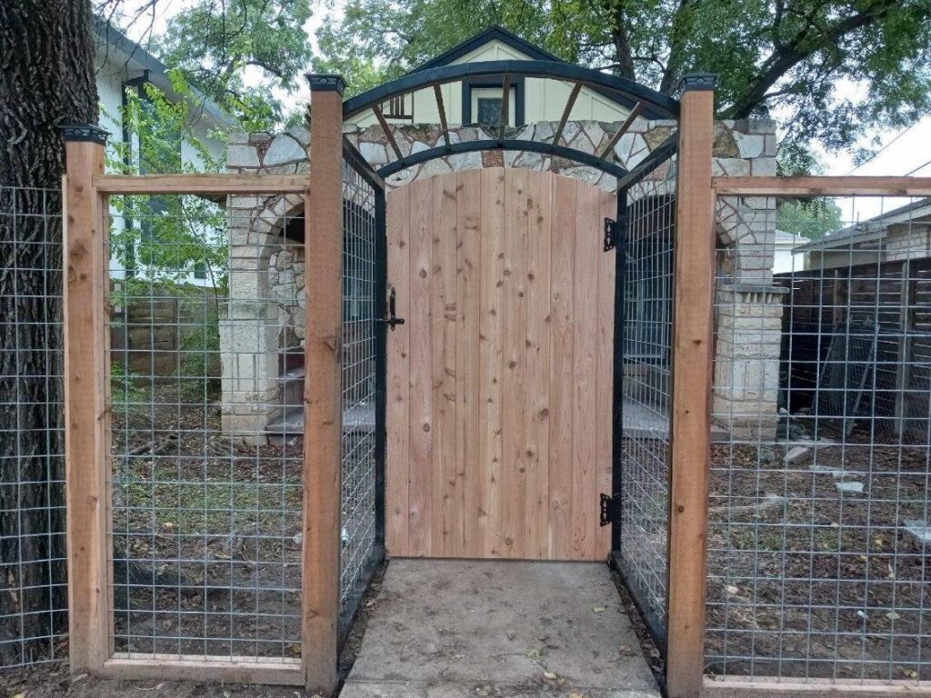 A decorative metal arch gate with a wooden gate and wire mesh fencing by Good Neighbor Fencing and Construction in Austin, TX.