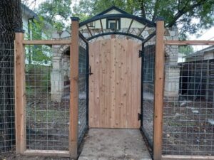 A decorative metal arch gate with a wooden gate and wire mesh fencing by Good Neighbor Fencing and Construction in Austin, TX.