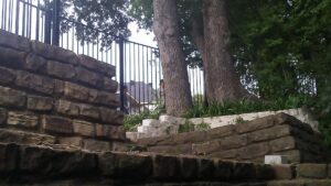 A decorative black metal fence installed on top of a stone retaining wall by Dallas Mobile Welder, LLC. in Dallas, TX.