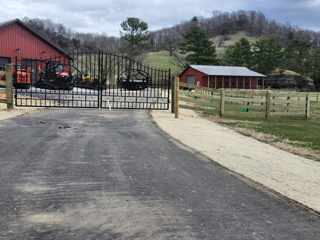 A decorative black metal gate and adjacent wooden rail fence installed by H&S Fencing & Supply in Linden, WI.