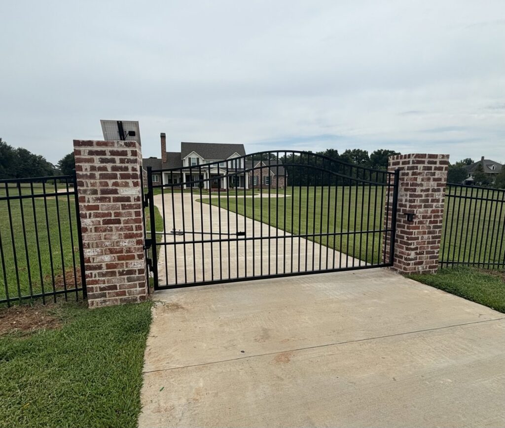 A decorative metal gate with brick pillars at a residential driveway entrance, installed by Lynch's Temporary Fencing & Dumpster rental in Bossier City, LA.